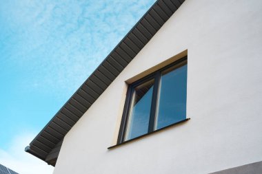 Modern bir evde mavi gökyüzünün altında ışık duvarlarıyla çerçevelenmiş büyük bir pencere bulunur..