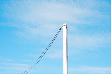 Güneşli bir günde mavi gökyüzüne doğru uzanan kabloları olan uzun bir elektrik direği..