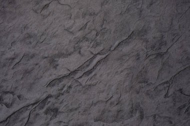 Koyu taşımsı yüzey karmaşık dokular ve doğal desenler sergiliyor..