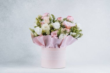 Pembe bir kutuya yerleştirilmiş gül ve yeşillikler içeren güzel bir buket..