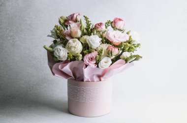 Dekoratif aksanlı yumuşak pembe bir kutuya dizilmiş çeşitli çiçeklerden çarpıcı bir buket..