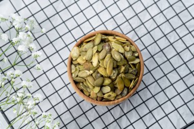 Kareli bir yüzeyde küçük çiçeklerle ahşap bir kasede dizilmiş kabak tohumları..