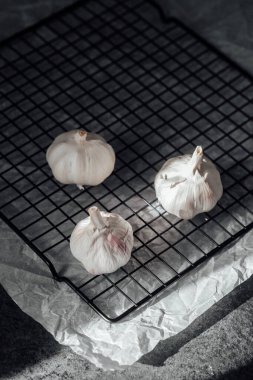 Üç sarımsak ampulü bir ızgara soğutma rafında duruyor, hafif ışıkla aydınlatılıyor..