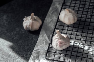 Üç sarımsak soğanı, iyi aydınlatılmış bir mutfakta, siyah bir soğutucunun üzerinde duruyor..