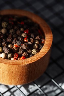 Tahta bir kasedeki çeşitli baharatlar, doğal ışıkta zengin renkler ve dokular sergiler..