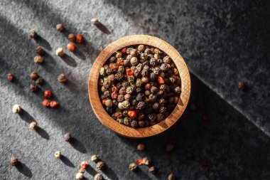 Çeşitli biber taneleri ahşap bir kaseyi doldurur, yumuşak gölgeler bırakır..