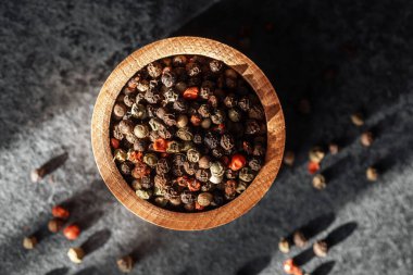 Değişik renklerde biberlerle dolu ahşap bir kase desenli bir taş yüzeyde oturur..