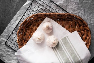 Hasır sepetin içindeki beyaz bir bezin üzerinde üç karanfil taze sarımsak dinleniyor..