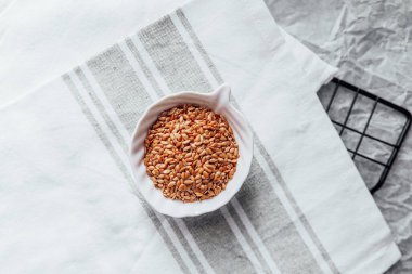 Keten tohumu beyaz bir kasede çizgili bir mutfak havlusunun üzerinde kullanıma hazır bekliyor..