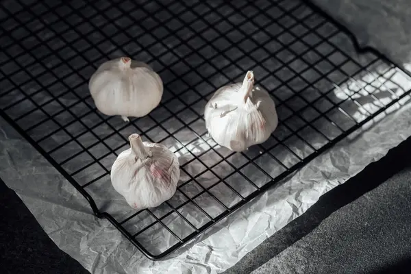 Taze sarımsak ampulleri, yumuşak ışığın altındaki tel soğutma rafında dinleniyor..