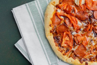 Taze domates dilimli lezzetli bir pepperoni pizza mutfak havlusunda duruyor..