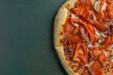 Biberli pizzanın üstüne koyu domates dilimleri serpiştirilmiş..