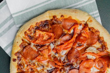 Kareli peçetede servis edilen domates dilimli taze pişmiş pepperoni pizzası..