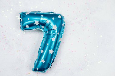 Yedi numaralı parlak mavi balon renkli konfetiyle açık bir yüzeyde duruyor..