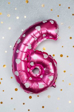 Gümüş kalpli altı numara şeklinde parlak pembe bir balon sergileniyor..