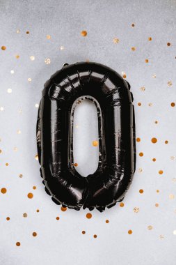 Gümüş bir yüzeye yerleştirilmiş siyah sıfır numaralı balon ve dağınık altın konfeti.