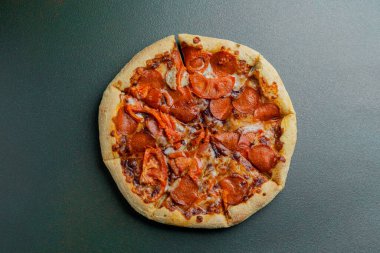 Eritilmiş peynirli ve kıtır kıtırlı, koyu bir yüzeye yerleştirilmiş nefis pepperoni pizza..