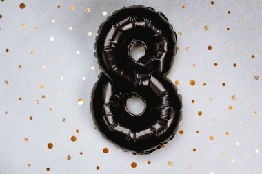 Büyük siyah bir sekiz numaralı balon altın konfetiyle benekli açık bir yüzeye yerleştirilir..
