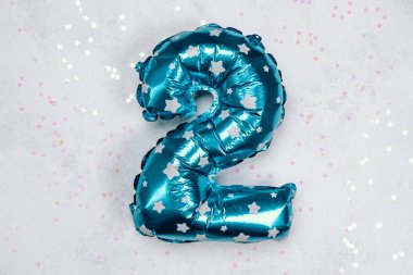 İki numara şeklindeki parlak mavi balon yıldızlı konfetilerin üzerinde duruyor..