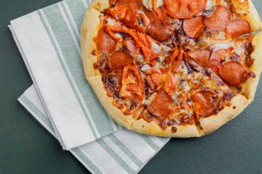 Biberli ve taze domatesli lezzetli bir pizza temiz bir peçetenin üzerinde duruyor..