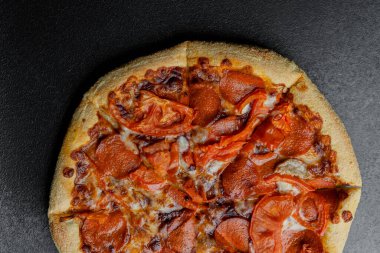 Pepperoni pizza, arka planda erimiş peynir ve taze domates dilimleri içerir..
