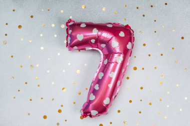 Parlak pembe yedi numaralı balon, parlak bir yüzeyde duran kalplerle süslenmiş..