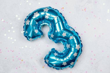 Üç numaralı parlak mavi balon renkli yıldızlarla dağılmış bir ışık yüzeyinde uzanıyor..