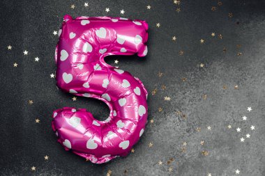 Beş yıldızlı pembe bir balon doğum günü için altın yıldızların arasında duruyor..