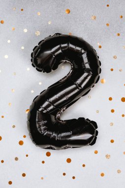 Siyah bir iki numaralı balon altın konfetiyle gümüş bir zemin üzerinde duruyor..