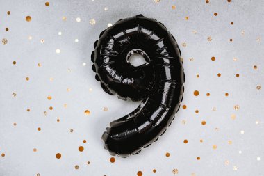 Dokuz numaraya benzeyen siyah bir balon altın noktaların ışıltılı zemininde duruyor..