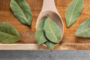 Taze defne yaprakları ahşap bir kaşıkta dinleniyor. Masada daha fazla yaprak var..