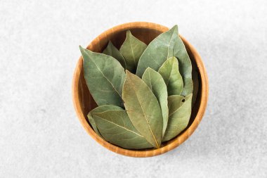 Kurumuş defne yaprakları tarafsız bir arka planda ahşap bir kasede düzgünce dizilmiş..