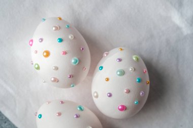 Parlak renkli yumurtalar bahar için hafif bir zemin üzerinde küçük boncuklarla süslenir..