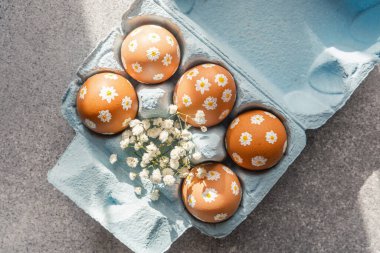 Çiçeklerle süslenmiş açık mavi bir karton içinde renkli çiçek yumurtaları..