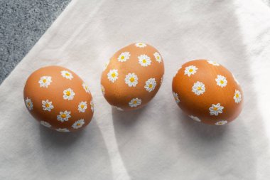 Üç kahverengi yumurta açık arkaplanda beyaz papatya desenleriyle süslenir..