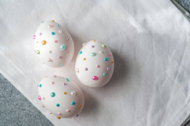 Renkli boncuklarla süslenmiş üç beyaz yumurta bir peçetede sergilenir..