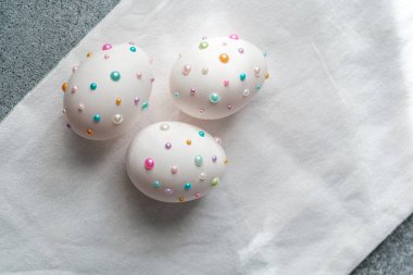 Üç güzel dekore edilmiş paskalya yumurtası hafif bir kumaşın üzerinde, canlı boncuklar sergiliyor..