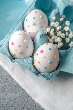 Renkli dekore edilmiş yumurtalar küçük beyaz çiçeklerin yanında turkuaz bir kutuda dinleniyor..