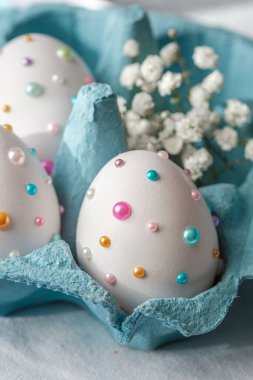 Canlı boncuklarla süslenmiş şık Paskalya yumurtaları ve narin çiçekler bir karton içinde otururlar..