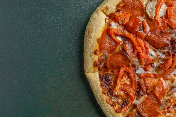 Biberli pizzanın üstüne koyu domates dilimleri serpiştirilmiş..