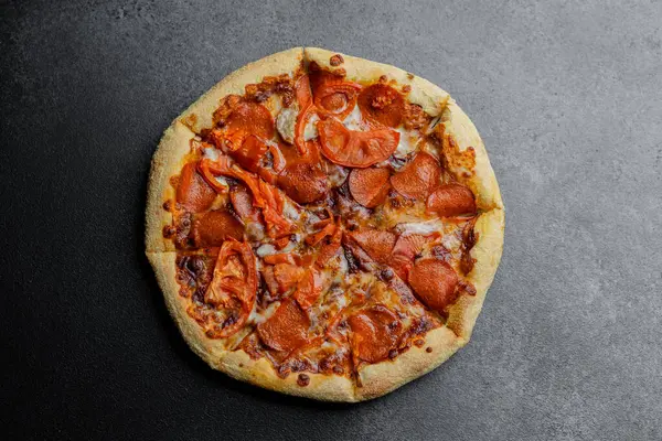 Taze pişmiş pepperonili pizza ve domates dilimleri karanlık bir yüzeyde tadını çıkarmaya hazır..