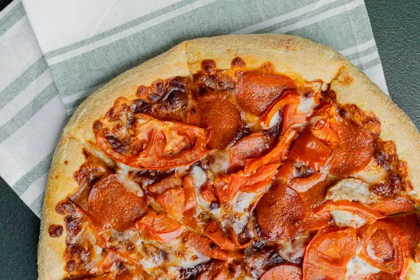 Kareli peçetede servis edilen domates dilimli taze pişmiş pepperoni pizzası..