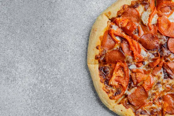 Gri arka planda domates dilimli taze pişmiş pepperoni pizza..