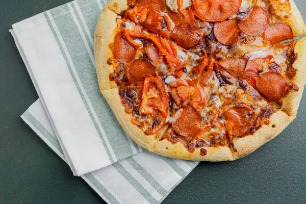 Biberli ve taze domatesli lezzetli bir pizza temiz bir peçetenin üzerinde duruyor..