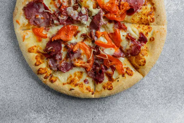 Çeşitli et ve sebzelerden oluşan dilimlenmiş pizza, gri bir arka planda servis ediliyor..