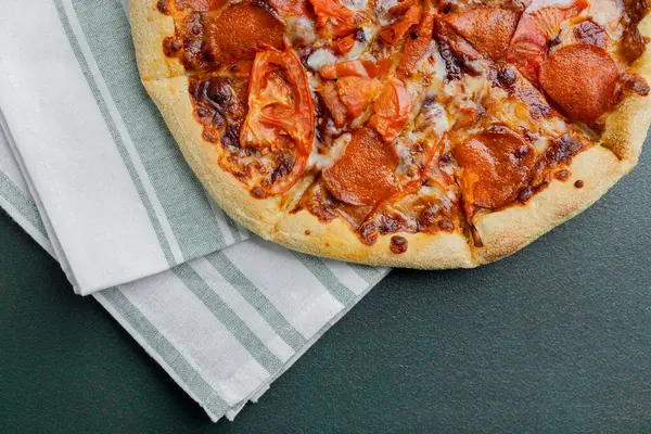 Taze domatesli lezzetli bir pepperoni pizzası çizgili bir kumaşın üzerinde duruyor..