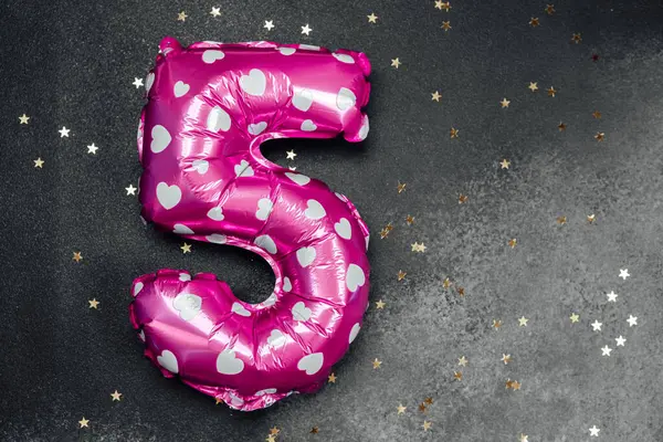 Beş yıldızlı pembe bir balon doğum günü için altın yıldızların arasında duruyor..