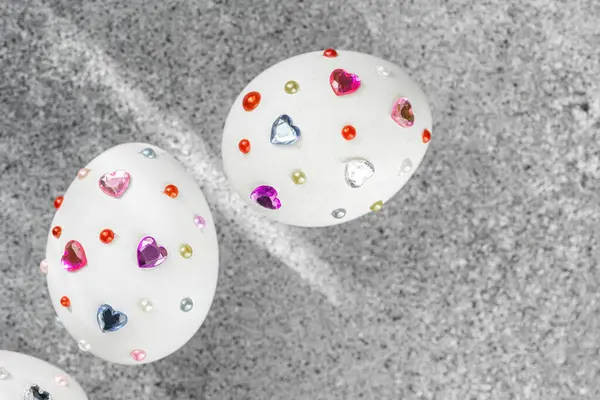 Renkli kalpler ve gri arka planda boncuklarla süslenmiş dekoratif beyaz yumurtalar..