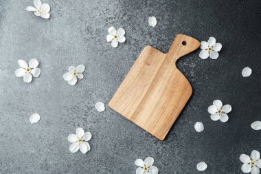 Koyu bir yüzeyde beyaz çiçek yapraklarıyla süslenmiş bir tahta doğrama tahtası var..