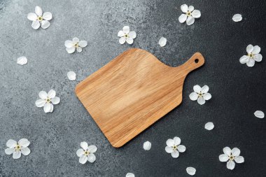 Tahta kesme tahtası, beyaz çiçeklerle süslenmiş koyu renkli bir yüzeye yerleştirilir..